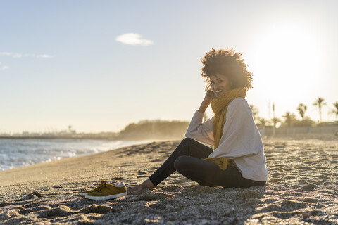 Frau sitzt bei Sonnenuntergang am Strand, lizenzfreies Stockfoto