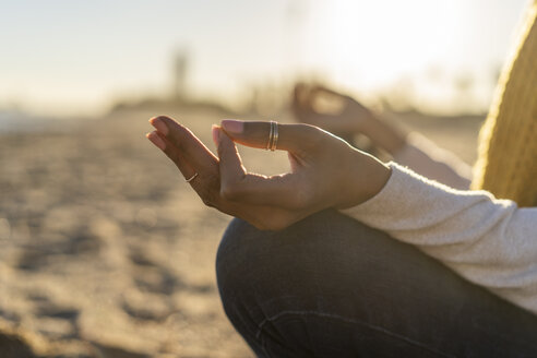 Woman sitting on the beach at sunset, meditating - AFVF02116