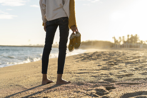 Barfüßige Frau am Strand, die ihre Schuhe trägt, lizenzfreies Stockfoto