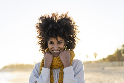 Porträt einer glücklichen Frau am Strand, die einen gelben Schal trägt, lizenzfreies Stockfoto
