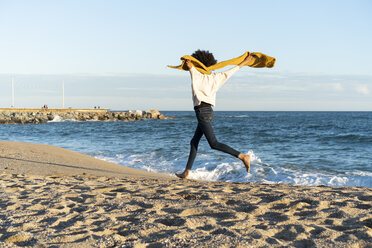 Woman running on the beach, wearing yellow scarf - AFVF02128