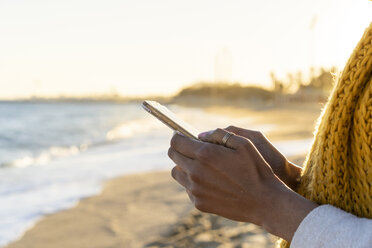 Frau mit gelbem Halstuch, die am Strand ihr Smartphone benutzt - AFVF02130