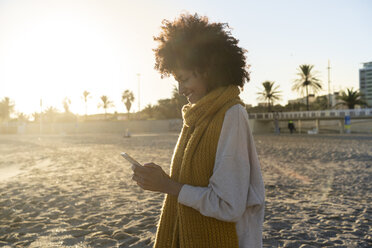 Frau mit gelbem Halstuch, die am Strand ihr Smartphone benutzt - AFVF02131