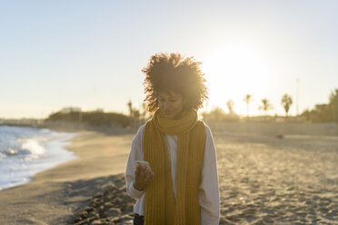Woman with yellow scarf, using smartphone on the beach - AFVF02134