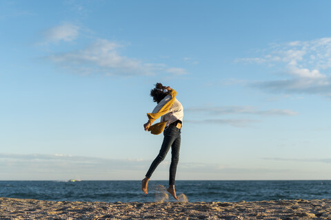 Frau springt am Strand, trägt Kopfhörer, hört Musik, lizenzfreies Stockfoto