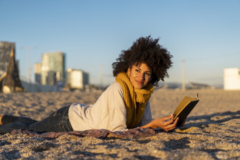 Frau liegt im Sand, entspannt am Strand, liest ein Buch, lizenzfreies Stockfoto