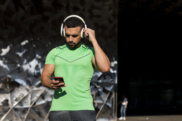 Sportive man during workout, using smartphone and headphones - MAUF01963