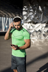 Sportlicher Mann beim Training, mit Smartphone und Kopfhörern - MAUF01964