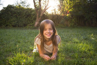Portrait of smiling little girl lying on a meadow at evening twilight - LVF07610