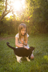 Lächelndes kleines Mädchen streichelt Katze im Garten - LVF07611