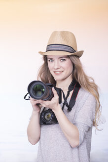 Portrait of smiling young woman comparing two different cameras - SKAF00082