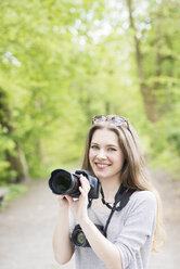 Porträt einer lächelnden jungen Frau, die zwei verschiedene Kameras im Freien vergleicht - SKAF00083