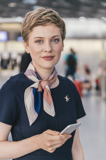Porträt eines selbstbewussten Angestellten einer Fluggesellschaft, der ein Handy am Flughafen hält - MFF04732