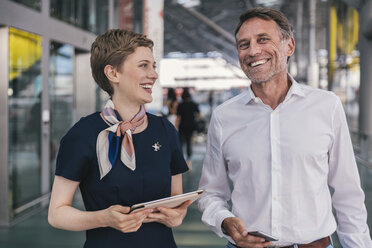 Glücklicher Mitarbeiter einer Fluggesellschaft mit Tablet und Passagier mit Mobiltelefon am Flughafen - MFF04738