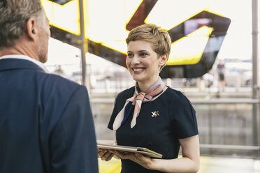 Lächelnder Mitarbeiter einer Fluggesellschaft mit Tablet im Gespräch mit einem Geschäftsmann auf dem Flughafen - MFF04769