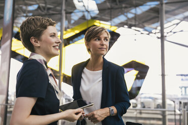 Lächelnder Mitarbeiter einer Fluggesellschaft mit Tablet und Geschäftsfrau auf dem Flughafen - MFF04771