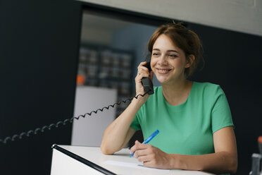 Lächelnde Frau, die im Büro mit einem Handy telefoniert - KNSF05423