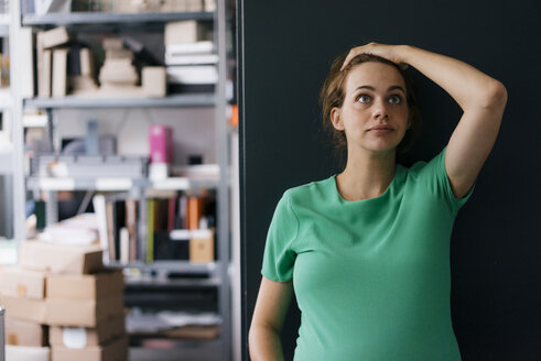 Schwangere Frau steht an einer Wand im Büro und schaut nach oben - KNSF05430