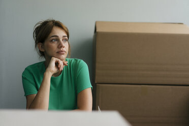 Thoughtful woman next to cardboard boxes in office - KNSF05434