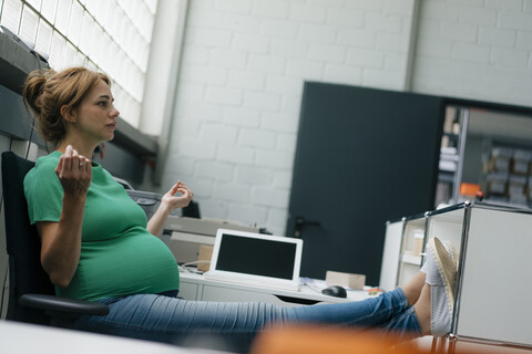 Schwangere Frau sitzt am Schreibtisch im Büro und macht eine Pause, lizenzfreies Stockfoto