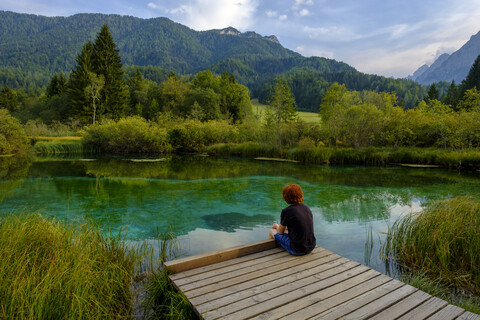 Slowenien, Gorenjska, bei Ratece, Sava Dolinka, Quelle, Zelenci-See, junger Mann sitzt auf Steg, lizenzfreies Stockfoto