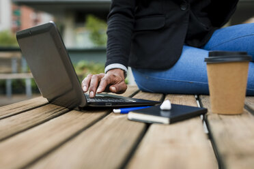 Geschäftsfrau sitzt auf einem Tisch im Freien und benutzt einen Laptop, Teilansicht - MAUF01980