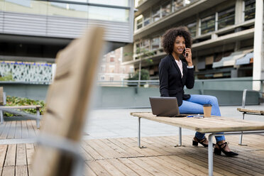 Businesswoman on the phone with laptop and coffee to go sitting on terrace - MAUF01981