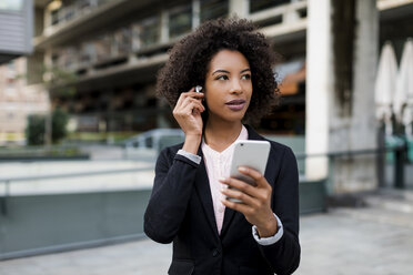 Portrait of businesswoman with smartphone putting on earphones - MAUF01983