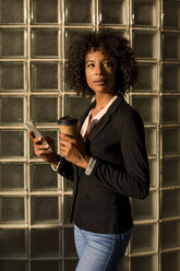 Portrait of businesswoman with coffee to go and cell phone at evening twilight - MAUF02002