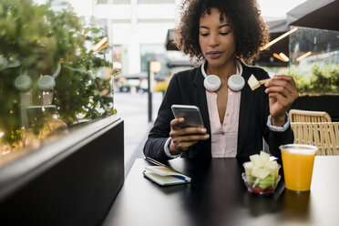 Porträt einer Geschäftsfrau, die in einem Straßencafé auf ihr Handy schaut, während sie einen Obstsalat isst - MAUF02019