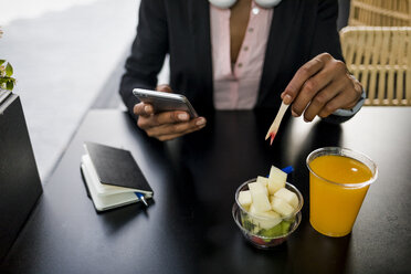 Geschäftsfrau, die in einem Straßencafé ein Mobiltelefon benutzt, während sie einen Obstsalat isst - MAUF02021