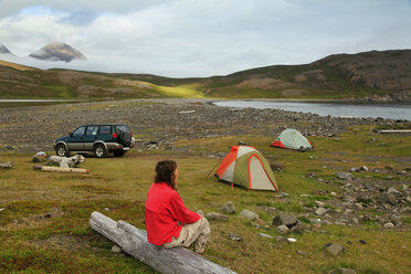 Woman sitting on log near camping tents and 4x4 car, Iceland - AURF07945