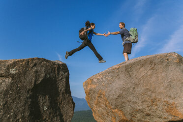 Man helping woman jump across boulder, Pitchoff Mountain, Adirondack Mountains, New York State, USA - AURF07954