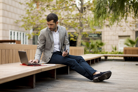 Businessman sitting on a bench using laptop stock photo