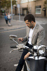 Businessman on motorscooter checking cell phone - MAUF02040