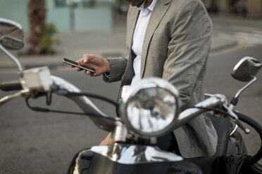 Close-up of businessman on motorscooter checking cell phone - MAUF02041