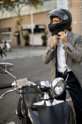 Businessman next to motorscooter putting on helmet - MAUF02045