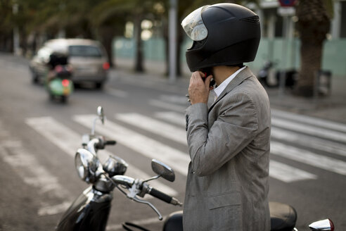 Businessman next to motorscooter putting on helmet - MAUF02046