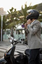 Businessman next to motorscooter putting on helmet - MAUF02047