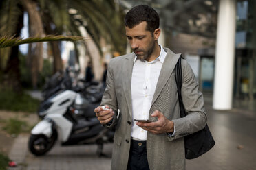 Businessman with cell phone in the city applying earbuds - MAUF02051