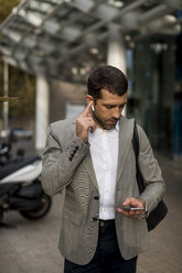 Geschäftsmann mit Mobiltelefon und Bluetooth-Kopfhörern in der Stadt - MAUF02052