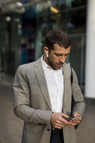 Geschäftsmann mit Mobiltelefon und Bluetooth-Kopfhörern in der Stadt, lizenzfreies Stockfoto