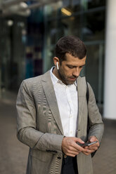 Businessman with cell phone and bluetooth earbuds in the city - MAUF02053