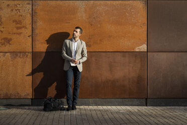 Businessman standing at a wall holding a notebook - MAUF02054