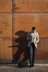 Businessman standing at a wall writing into notebook - MAUF02055