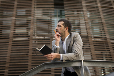 Businessman standing in the city holding a notebook - MAUF02060