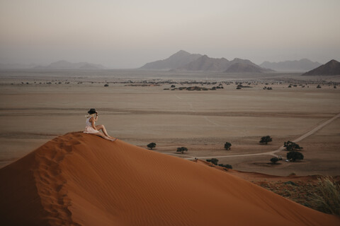 Namibia, Namib-Wüste, Namib-Naukluft-Nationalpark, Sossusvlei, Frau sitzt bei Sonnenuntergang auf der Elim-Düne, lizenzfreies Stockfoto