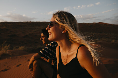 Namibia, Namib-Wüste, Namib-Naukluft-Nationalpark, Sossusvlei, glückliches Paar sitzt bei Sonnenuntergang auf der Elim-Düne, lizenzfreies Stockfoto