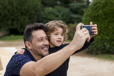 Happy father and son on taking a selfie in park - MAUF02071