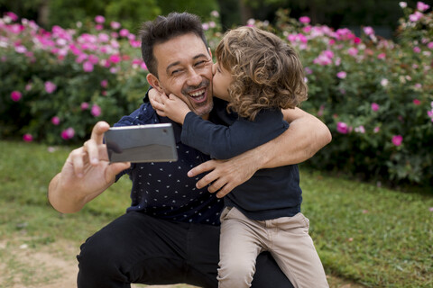 Happy father and son on taking a selfie in park stock photo